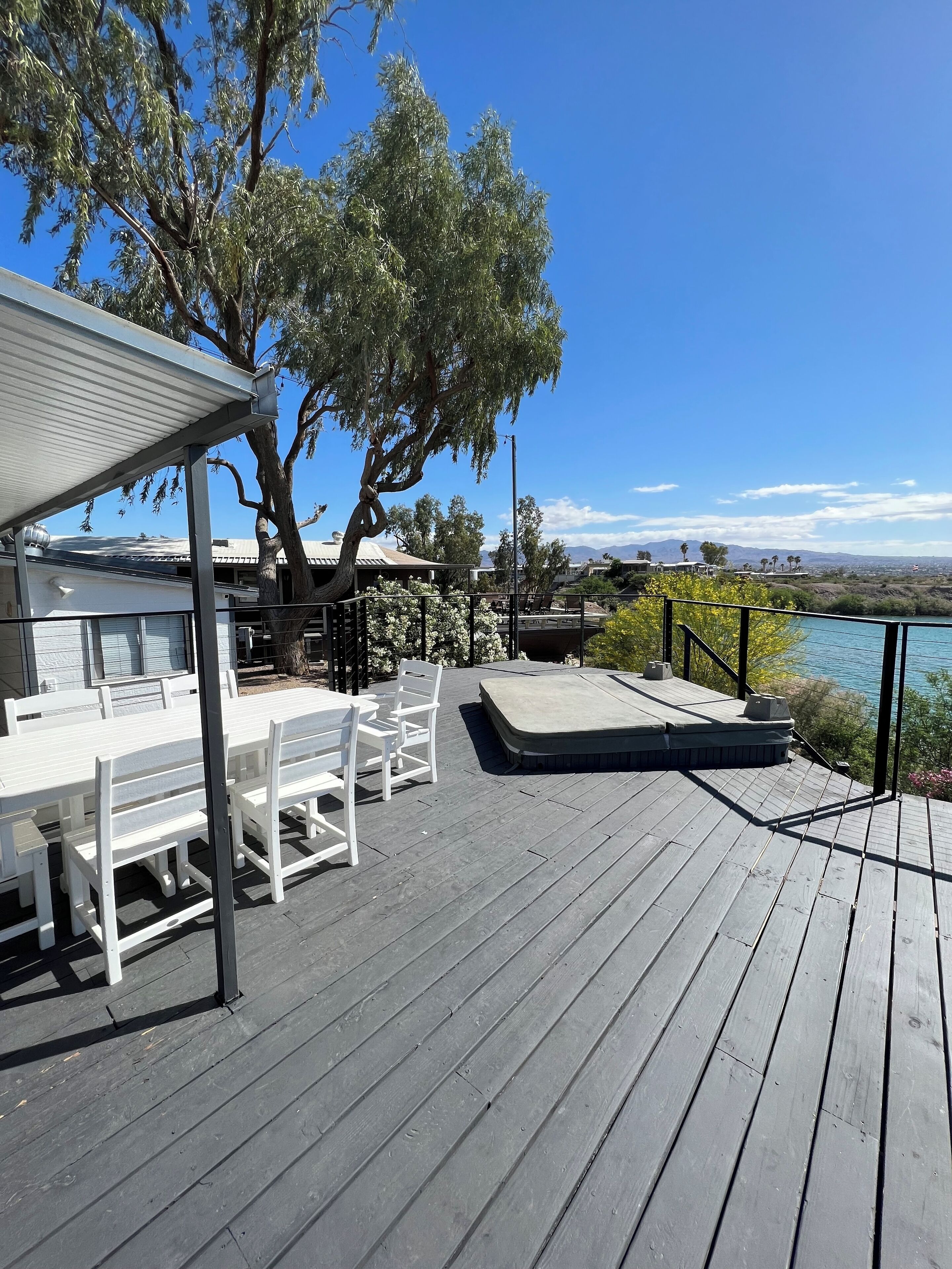 A deck with white chairs and a table, overlooking a body of water with mountains in the distance.