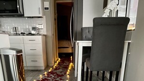 Una cocina con armarios blancos, un bote de basura de acero inoxidable y una zona de comedor con una silla gris y una mesa.