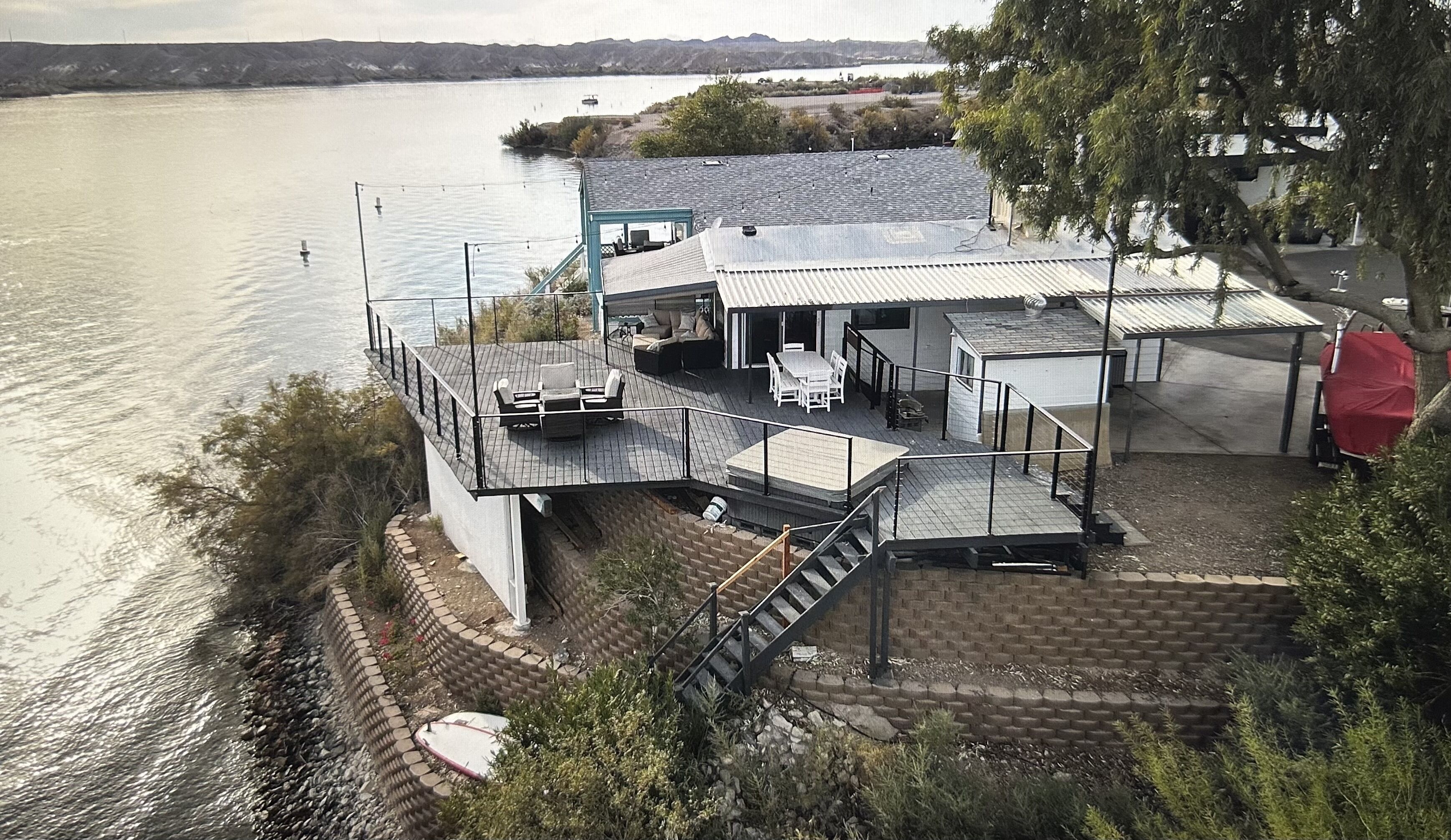 A waterfront property with a deck, outdoor seating, and a staircase leading to a covered area.