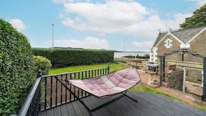 A wooden deck with a cushioned chair, a hedge, and a building with a cross on the roof.
