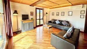 A spacious living room with a wooden ceiling, a grey sofa, a coffee table, and a TV on a cabinet.
