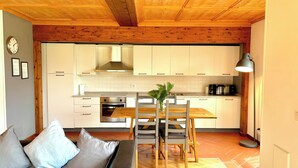 A modern kitchen with wooden ceiling beams, white cabinets, and a dining area with a wooden table and chairs.
