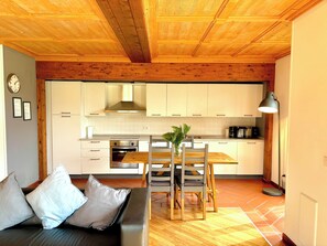Eine moderne Küche mit Holzbalkendecke, weißen Schränken und einem Essbereich mit Holztisch und Stühlen.