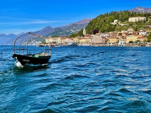Ein Boot namens 'CREVIA' auf ruhiger See mit einer Küstenstadt und Bergen im Hintergrund.