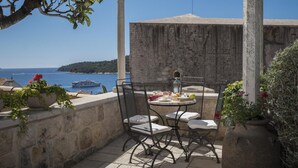 Une terrasse extérieure avec une table et des chaises, offrant une vue sur un plan d’eau et un bâtiment historique.