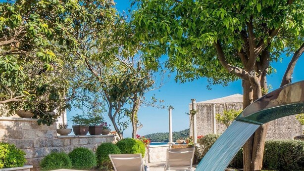 Une piscine agrémentée d’une cascade, entourée de murs en pierre et de plantes en pot.