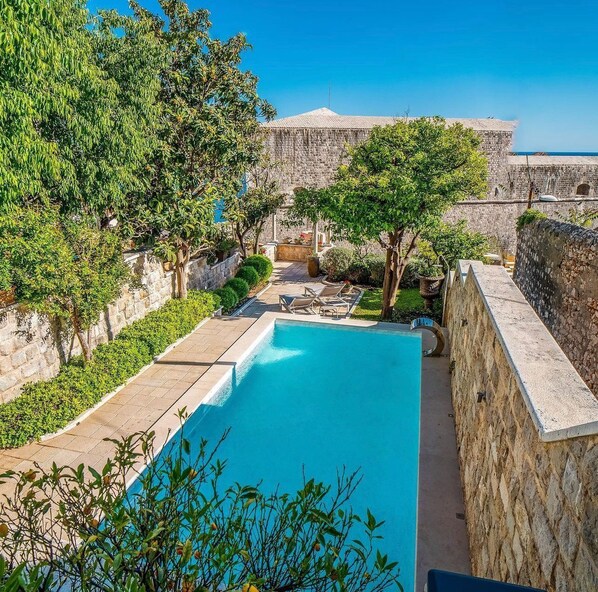 A pool area with a stone wall, trees, and a view of a historic building.