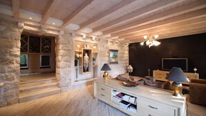 Un vaste salon avec des murs en pierre, des poutres en bois, une cheminée et un téléviseur.