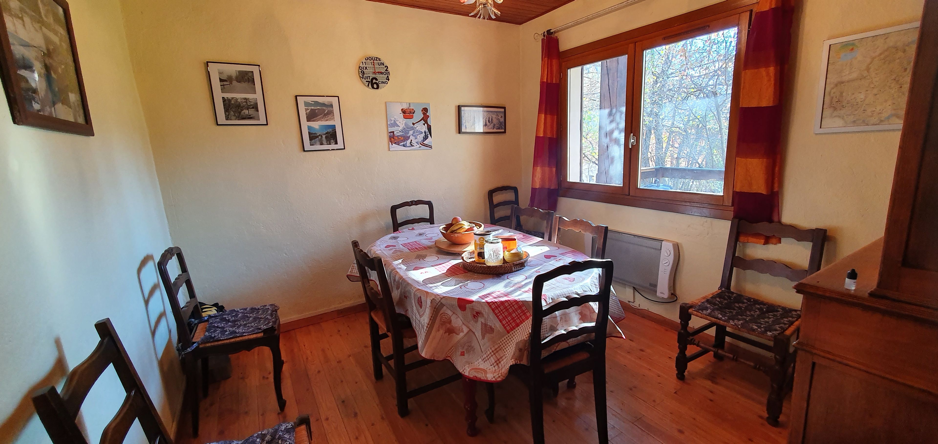 Une salle à manger avec une table dressée pour quatre personnes, des chaises, un radiateur et une fenêtre avec des rideaux.