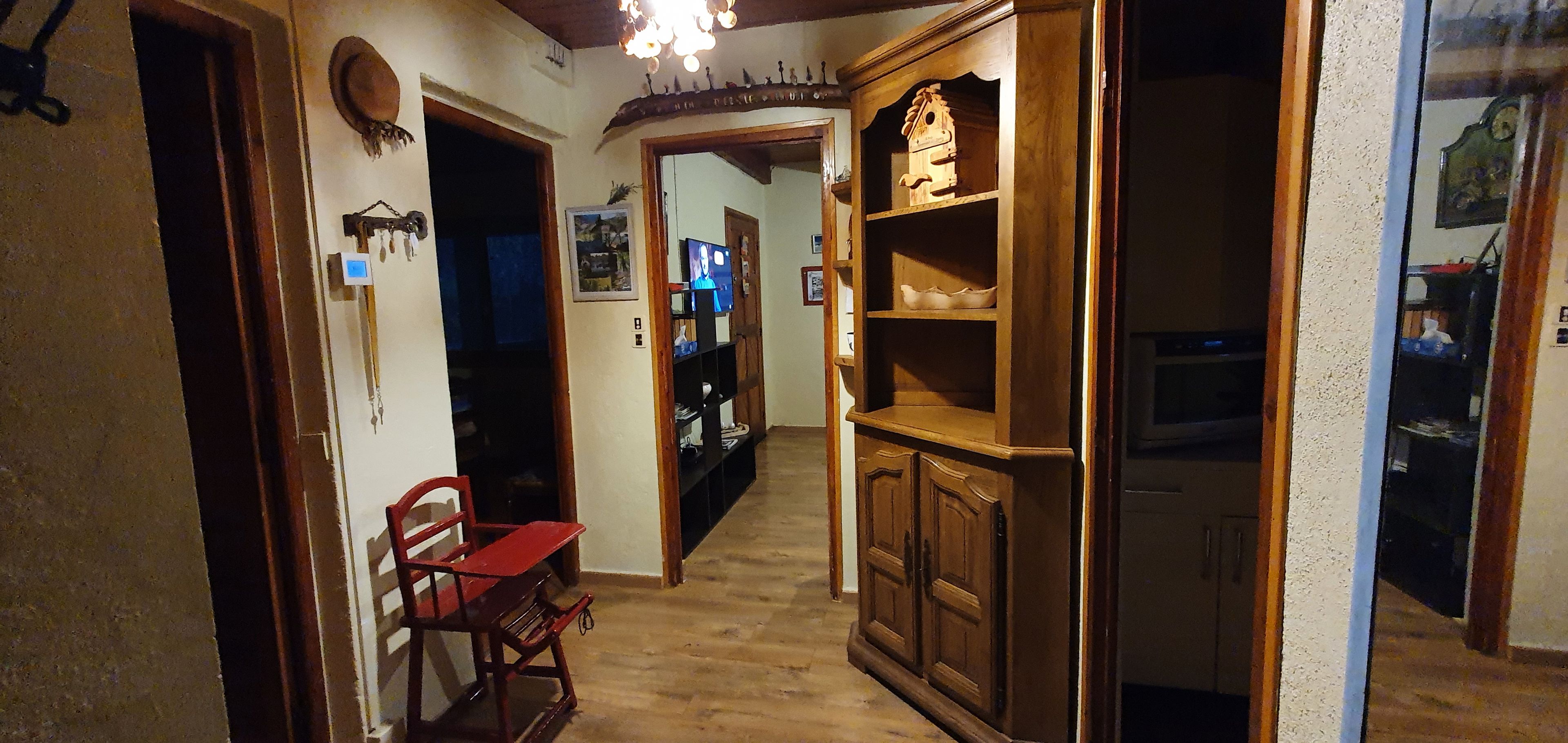 A narrow hallway with wooden flooring, a red chair, a wooden cabinet with shelves, and a ceiling light fixture.