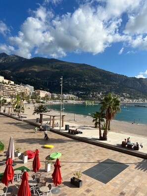 A coastal view with a beach, palm trees, and a mountain in the background. - Menton Studio Near the Ocean (Menton)