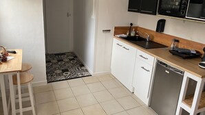 Eine kleine Küche mit weißen Schränken, einer Mikrowelle, einem Spülbecken und einem Essbereich mit Tisch und Hocker.