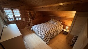 A cozy attic bedroom with a wooden floor, a checkered bedspread, a small bedside table with a lamp, and a Christmas tree. - Individual cottage 10-12 person  (Châtel)