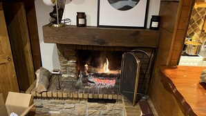 A fireplace with a stone surround, a mantel with decorative items, and a wooden bench. - Individual cottage 10-12 person  (Ch âtel)
