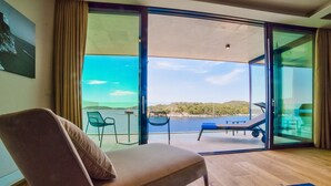 A room with a large sliding glass door leading to a balcony with a view of a body of water and hills. - PureLuxuryExclusiveVillaStateOfTheArtVillaExcellentLocationPrivateBeach (Zaton)