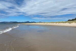 A wide sandy beach with gentle waves, a clear sky, and distant mountains. - 2 Bed Cottage Sleeps 4 - Pets Ok - Private Garden (Penrhyndeudraeth)