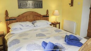 Ein Schlafzimmer mit einem Holzkopfteil, einem floralen Bettbezug, einem Gemälde mit Meereslandschaft, einer Lampe und einem zusammengerollten Handtuch auf dem Bett.