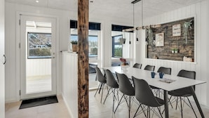 A modern dining area with a white table, black chairs, and a wooden accent wall. - 3 bedroom amazing home in Storvorde (Storvorde)
