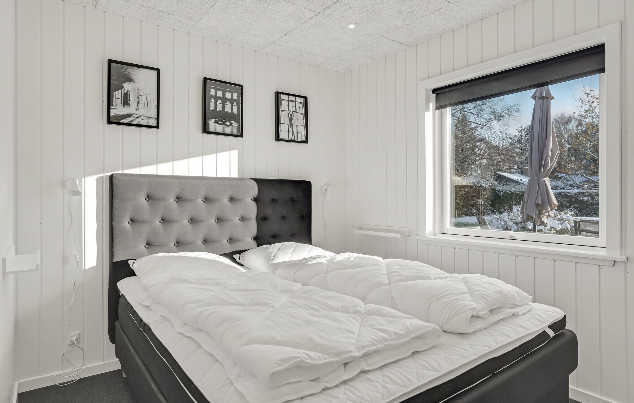 Ein Schlafzimmer mit einem Bett, einem Fenster mit Blick auf verschneite Landschaft und drei gerahmten Bildern an der Wand.