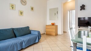 Un salon avec un canapé bleu, une commode en bois, un téléviseur à écran plat et des horloges fixées au mur.