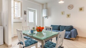 Un coin repas avec une table en verre, des chaises blanches, un canapé bleu et un radiateur fixé au mur.