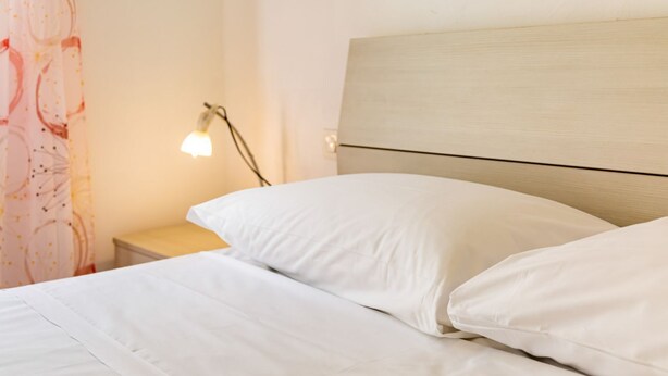 Un lit avec une literie blanche, une tête de lit en bois et une lampe de chevet.
