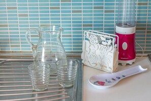 Una encimera de cocina con una jarra, vasos, una licuadora y una bandeja decorativa.