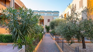 A pathway flanked by buildings with balconies, surrounded by greenery and a fence. - Bright and comfortable apartment, able to accommodate up to 4 people, with a large double bedroom and bedroom with a bunk bed, equipped terrace, living room and kitchenette. Ideal for a relaxing beach holiday, a few meters from the Blue Beach and in a co (Marotta)