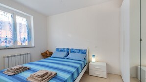 A bedroom with a bed, a nightstand, a lamp, a window with curtains, and a radiator. - Bright and comfortable apartment, able to accommodate up to 4 people, with a large double bedroom and bedroom with a bunk bed, equipped terrace, living room and kitchenette. Ideal for a relaxing beach holiday, a few meters from the Blue Beach and in a co (Marotta)