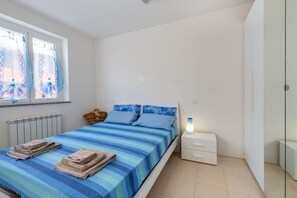 Une chambre à coucher comprenant un lit, une table de chevet, une lampe, une fenêtre avec des rideaux et un radiateur.