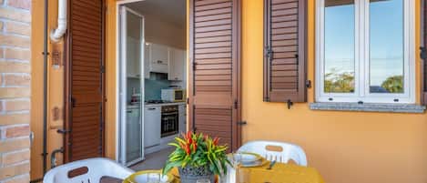 Un coin repas avec une table dressée pour quatre personnes, une plante en pot et une vue sur la cuisine par une porte ouverte.