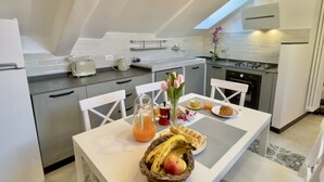 Eine moderne Küche mit weißen Schränken, einem Esstisch mit Stühlen und einer Frühstücksvorrichtung, darunter eine Obstkorb, Waffeln und ein Glas Orangensaft.
