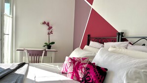 Ein Schlafzimmer mit einem Bett, Kissen, einem Schreibtisch, einem Stuhl und einer Topforchidee.