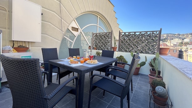 Eine Dachterrasse mit einem für das Frühstück gedeckten Tisch, darunter Croissants und Orangensaft, umgeben von Korbstühlen.