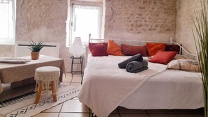 A bedroom with a bed, a small table with a plant, a lamp, and a window. - 🌊 5 mn plage 🌴 Proche LA ROCHELLE - Charmant T2 🏡 4 Pers. (Salles sur Mer)