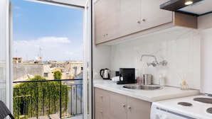 A modern kitchen with a large window, a balcony with a chair, and a view of the cityscape. - City Panorama - One Bedroom Apartment (Corfu)