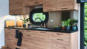 A modern kitchen with wooden cabinets, a black countertop, and a window with a view of greenery.