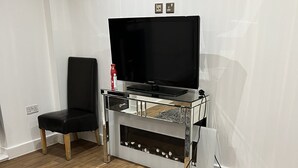 Ein modernes Wohnzimmer mit einem Flachbildfernseher auf einem Glastisch, einem schwarzen Ledersessel, einem grauen, flauschigen Teppich und Holzböden.