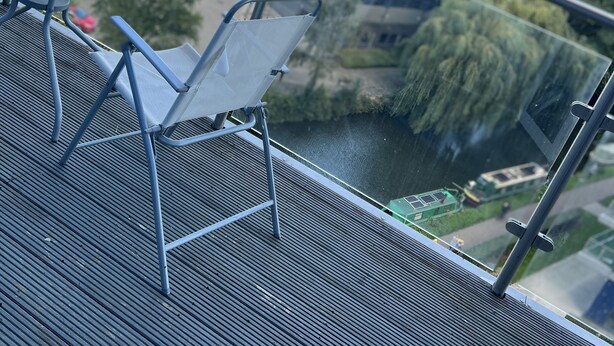 Ein Balkon mit Tisch und Stühlen mit Blick auf einen Fluss und Gebäude.