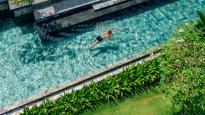 Una cabaña sobre el agua con piscina, un área de estar cubierta y abundante vegetación.