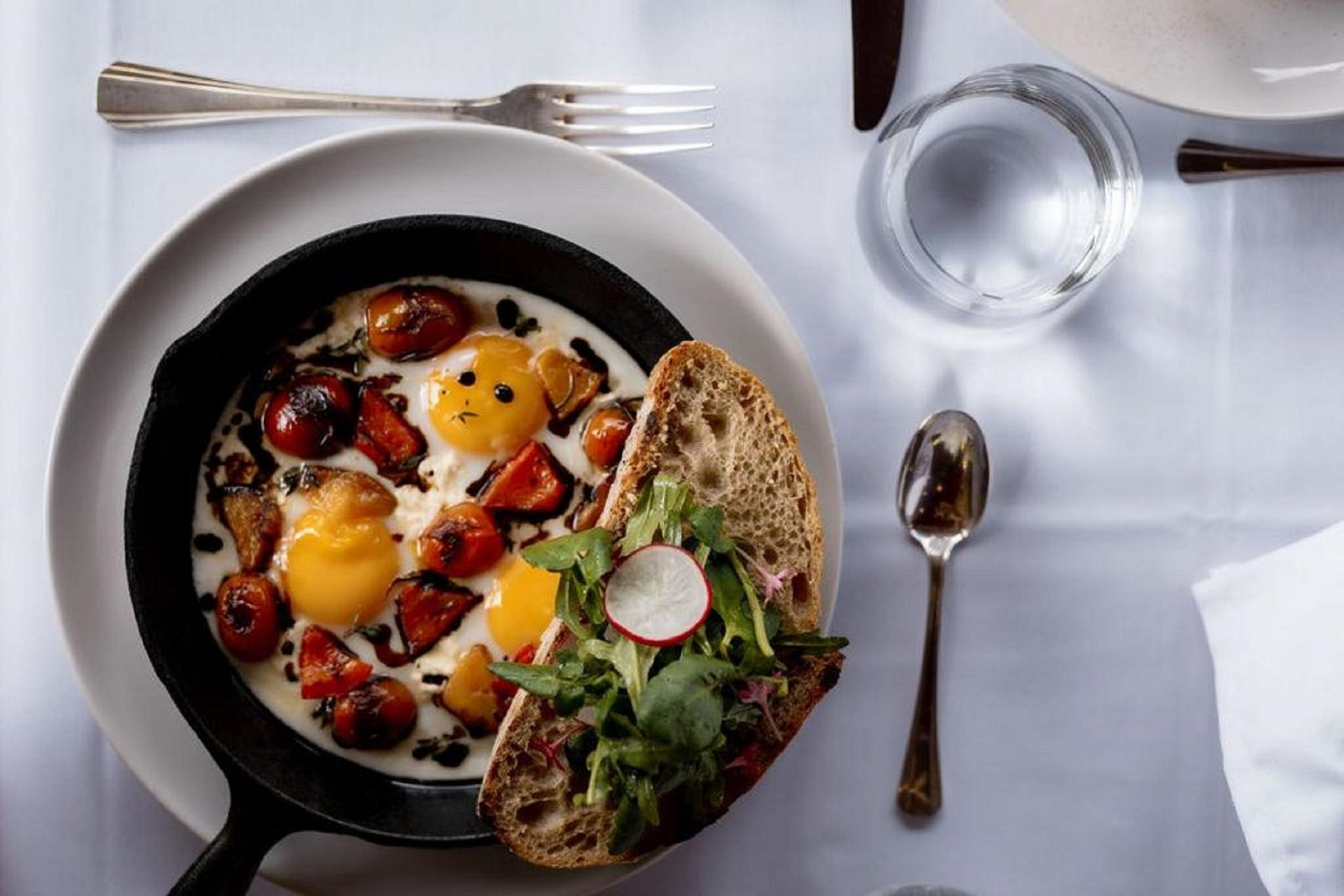 A breakfast dish with eggs, tomatoes, and bread on a white plate.