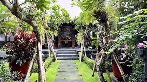 Un sendero de jardín que conduce a un edificio con una entrada tradicional, rodeado de exuberante follaje y faroles colgantes.