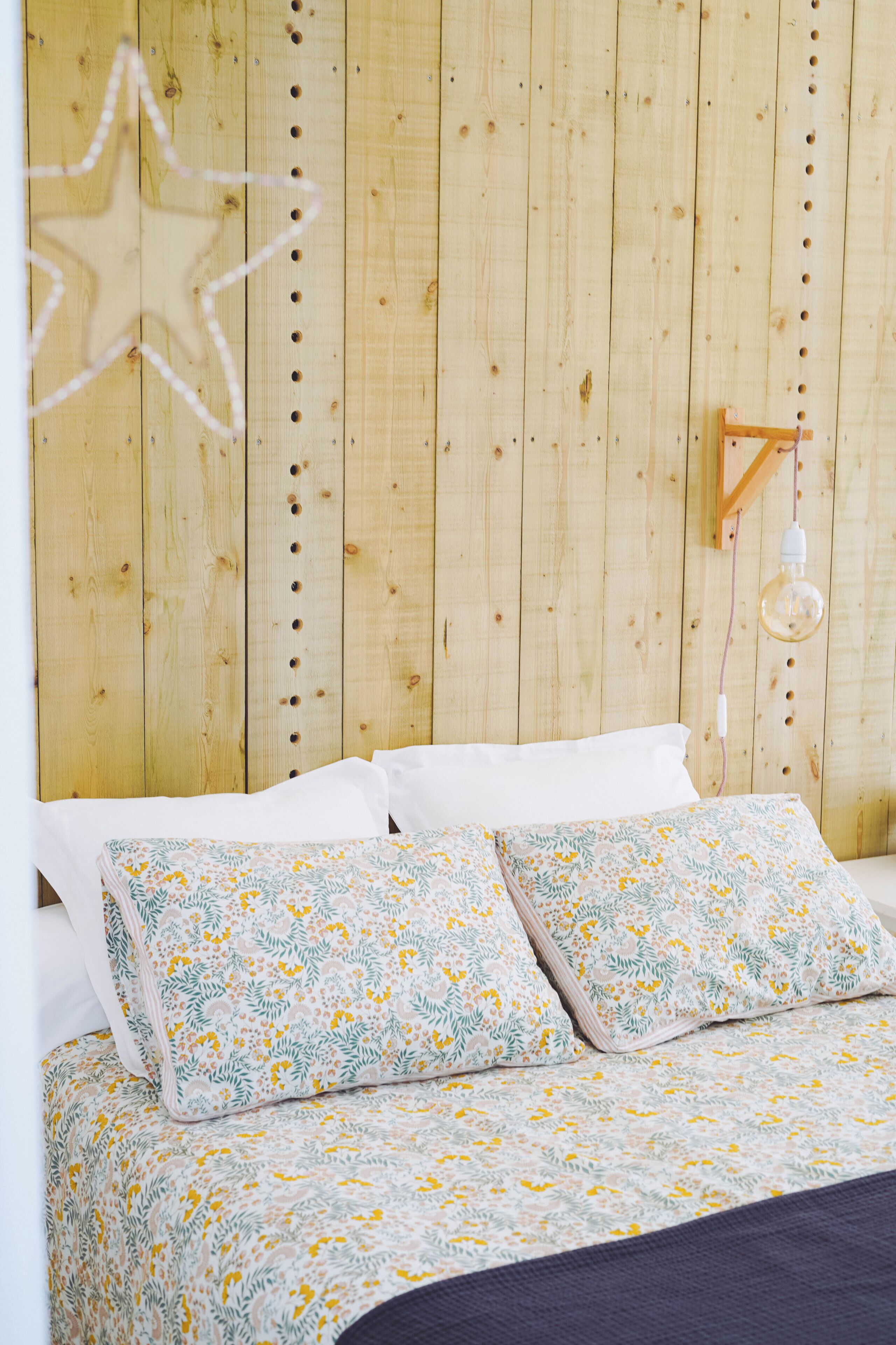 A wooden-paneled room with a bed, pillows, a hanging light fixture, and a star decoration.