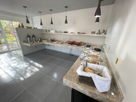 Una cocina moderna con encimeras de granito, luces colgantes negras y diversas opciones para el desayuno.