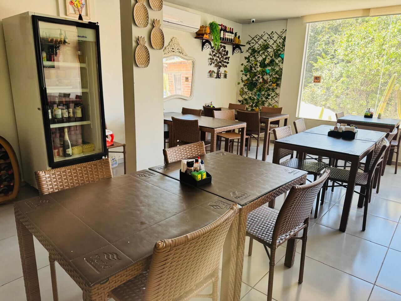 A dining area with a large wooden table and wicker chairs, a refrigerator, and decorative wall items.