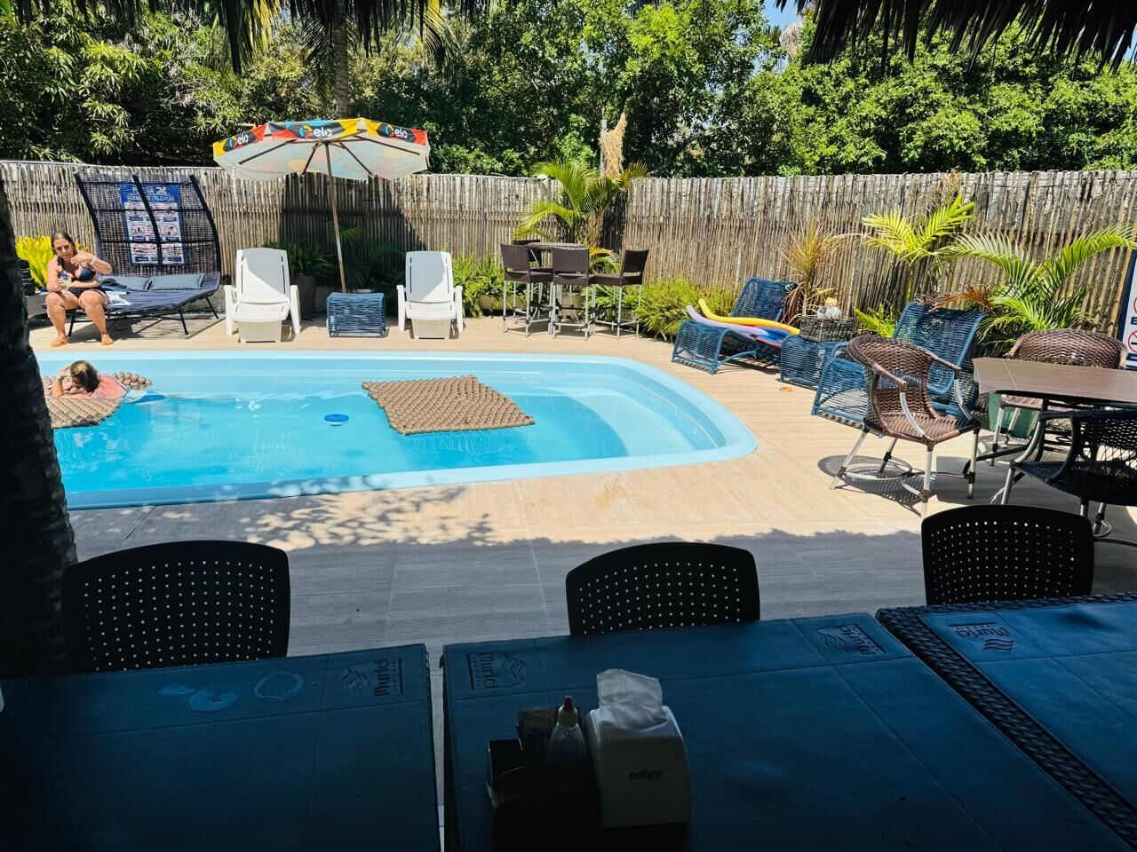 A backyard with a swimming pool, lounge chairs, and a table with umbrellas.