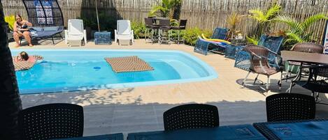 A backyard with a swimming pool, lounge chairs, and a table with umbrellas.