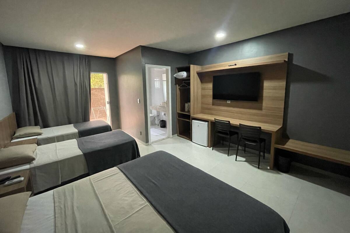 A hotel room with two single beds, a small desk with a chair, a television mounted on the wall, and a door leading to a bathroom.