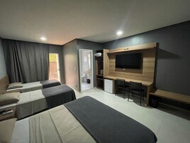 Una habitación de hotel con dos camas individuales, un pequeño escritorio con una silla, un televisor montado en la pared y una puerta que da al baño.