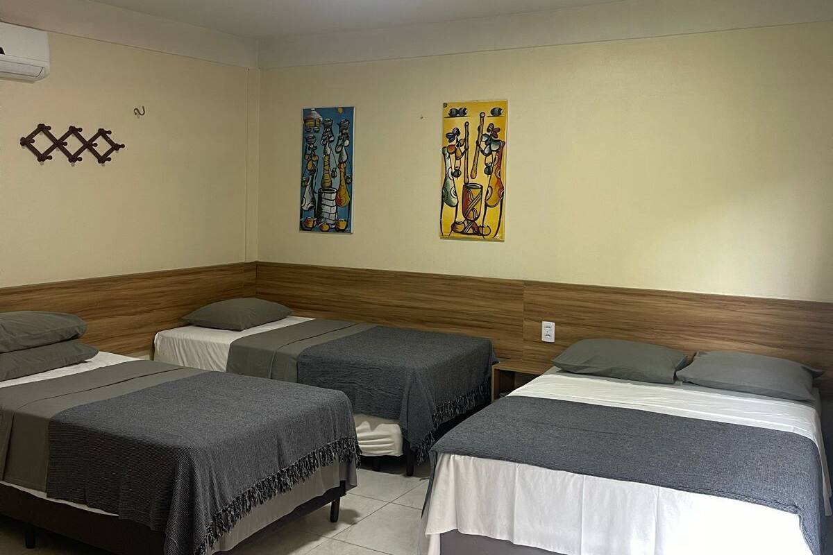 A hotel room with four beds arranged in a row, a wooden headboard, a tiled floor, and two wall art pieces.